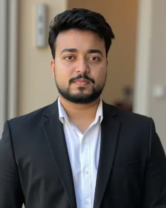 "A young man with short black hair and a neatly trimmed beard, wearing a black blazer over a white shirt, looking confidently at the camera."